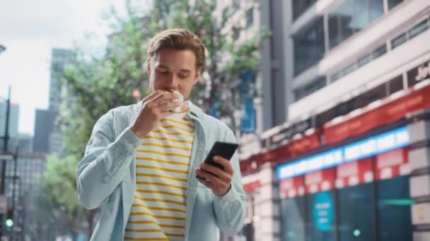Hombre guapo comiendo hamburguesa y el uso de Smartphone en la ciudad — Vídeos de Stock