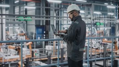 Araba fabrikasında dizüstü bilgisayarı olan bir erkek mühendis.