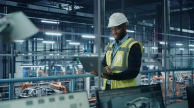 Otomobil fabrikasında erkek mühendis dizüstü bilgisayar kullanıyor.