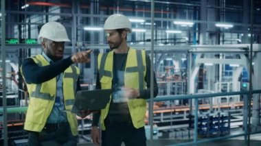 İki mühendis otomobil fabrikasında dizüstü bilgisayar kullanıyor.