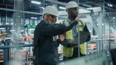 İki mühendis otomobil fabrikasında dizüstü bilgisayar kullanıyor.