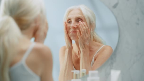 Mujer mayor usando el espejo de crema facial — Vídeos de Stock