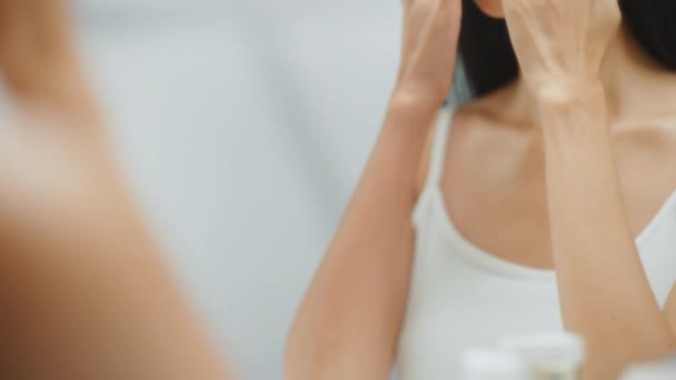 Jovem mulher adulta usando creme facial e espelho — Vídeo de Stock