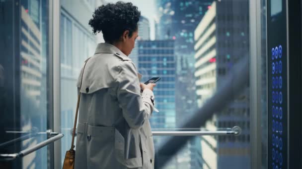 Латинська жінка їзда ліфт до офісу за допомогою смартфона — стокове відео