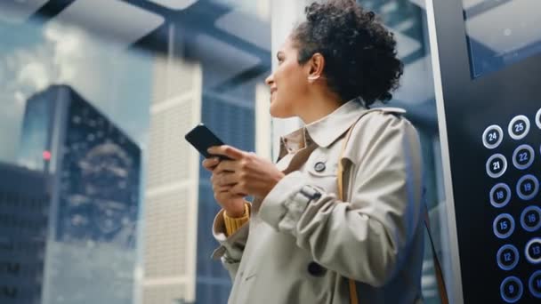 Lateinamerikanerin fährt mit Smartphone im Fahrstuhl ins Büro — Stockvideo