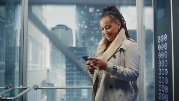 Чорна жінка їзда ліфт до офісу за допомогою смартфона — стокове відео