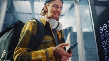 Yemek dağıtan adam asansöre biniyor. Akıllı telefon kullanıyor.