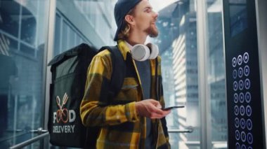 Yemek dağıtan adam asansöre biniyor. Akıllı telefon kullanıyor.