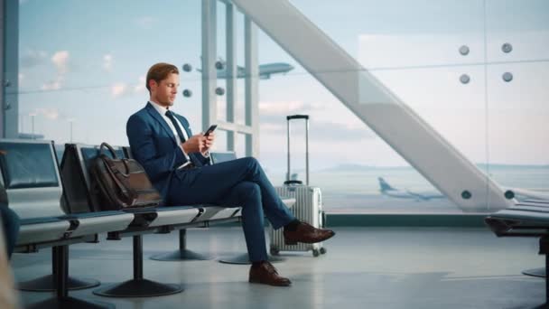 Бизнесмен использует смартфон в ожидании в терминале аэропорта — стоковое видео