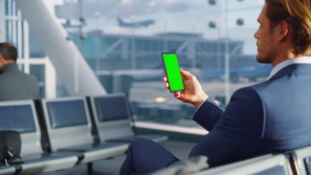 空港でグリーンスクリーンスマートフォンを使うビジネスマン — ストック動画