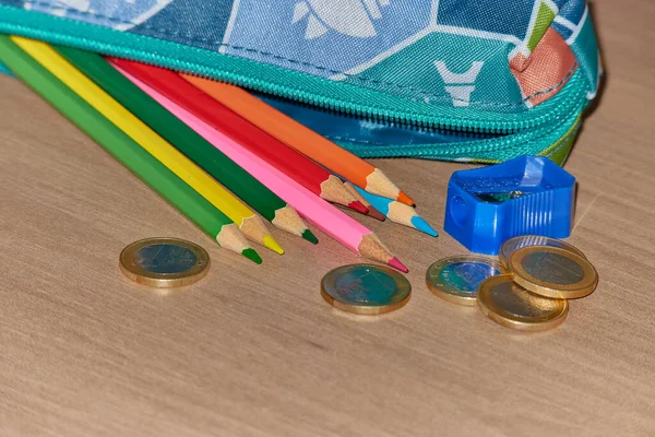Close-up of crayons next to a pencil case, a pencil sharpener and some coins.Tthe price of education concept