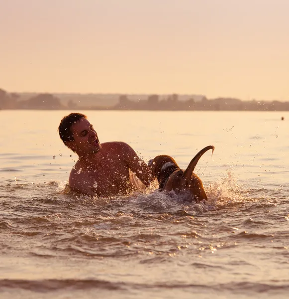 Man met kleine beagle pup gek rond in oceaan zonsondergang golven — Stockfoto