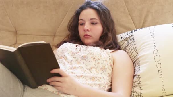 Menina lê livro best-seller no sofá confortável — Vídeo de Stock
