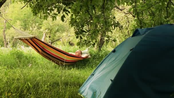 Gelukkig man ontspannen in een hangmat in de zomerkamp — Stockvideo