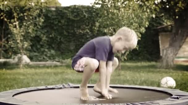 Fröhlich blonden Jungen springen auf dem Trampolin im Sommergarten — Stockvideo