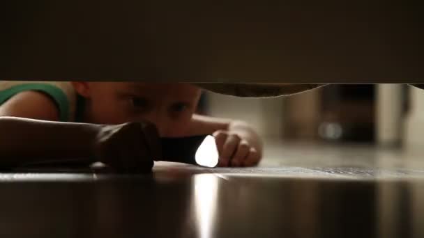 Little boy something finding under the bed with flashlight — Stock Video