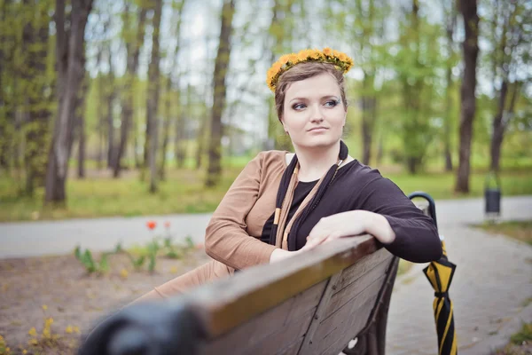 彼女の頭の上に黄色の花の花輪と座っている女の子 — ストック写真