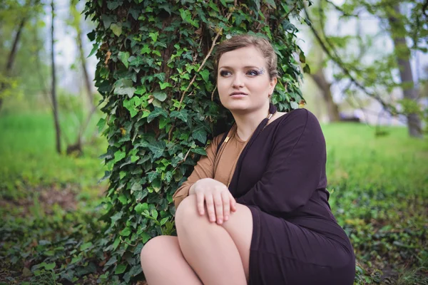Siyah ve kahverengi elbiseli kız bir ağacın yanında oturur — Stok fotoğraf