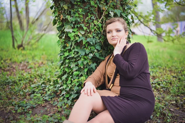 Siyah ve kahverengi elbiseli kız bir ağacın yanında oturur — Stok fotoğraf