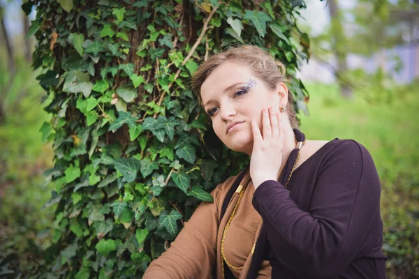 Girl in black and brown dress sits near a tree — Stock Photo, Image