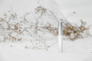 Herhangi bir yazı olmadan kozmetik, hijyen veya tıbbi ürünler için bir beyaz şişe veya tüp, kurumuş çiçekli hafif bir arkaplan üzerine yazı.