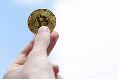 Elinde altın bir Bitcoin sembolü, temiz bir gökyüzü arkaplanı, kopyalama alanı var. BTC madeni para, kripto para kişisel finans, kripto para birimi borsa ticaret konsepti, bir kişi, birinci şahıs pov