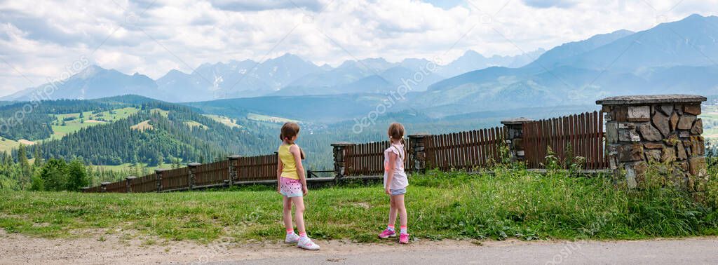 Two young children, elementary age girls standing in front of full Polish Tatra mountain range, high resolution panorama. Kids travel and exploration lifestyle, trip destinations, Europe, Poland