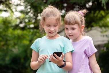 İki ilkokul öğrencisi kız, kız kardeş, çocuklar gülüyorlar, akıllı telefon, cep telefonu, portre, dışarıda eğleniyorlar, teknoloji meraklısı çocuklar, sıradan teknoloji kavramı gerçek insan yaşam tarzı