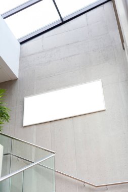 Modern bir şirket koridorunda beton bir duvara asılı boş beyaz dikdörtgen reklam çerçevesi, hiç kimse. İş geliştirme iç merdiven geniş çerçeve şablonu, modelle.