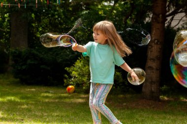 Mutlu bir ilkokul çocuğu, sabun köpüğüyle oynayan bir kız dışarıda, yaz, mutluluk patlatan bir kişi, eğlence, çocukluk enerjisi, hareket konsepti, insanların yaşam tarzı.