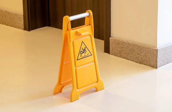 One orange caution slippery wet floor fold out sign in the hallway, workplace safety, accidents symbol, risk of falling, warning abstract concept, nobody, single object closeup, no people, maintenance
