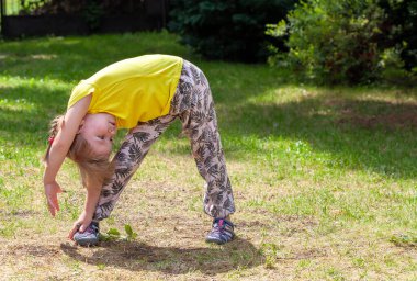 Okul çağındaki bir çocuk, egzersiz yapan bir kız, bahçede esneme hareketleri, arka bahçede fiziksel egzersiz, esneme hareketleri. Çocuklar formda, sağlıklı aktif çocukluk sağlık yaşam tarzı basit bir kavram, yaz