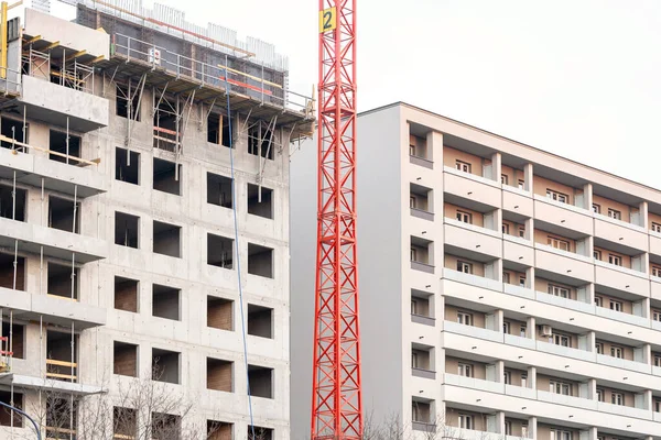 Housing development concept, generic block of flats under construction, unfinished apartment building next to a brand new finished one, two different buildings, nobody, construction crane in between