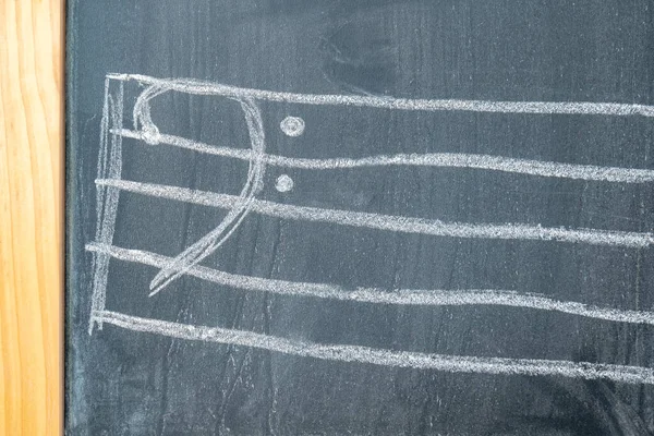 Bass clef hand drawn by a child on a classic traditional chalkboard, front view, nobody, no people. Bass clef simple white chalk drawing closeup, music symbols, musical education abstract concept