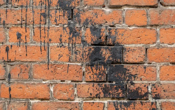 Simple old weathered brick wall splashed with black paint, tar, backdrop, background texture, wallpaper, nobody. Building side worn bricks black paint splash wall front view, closeup, no people