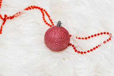 Kabarık beyaz arka planda boncukları olan kırmızı bir Noel topu..