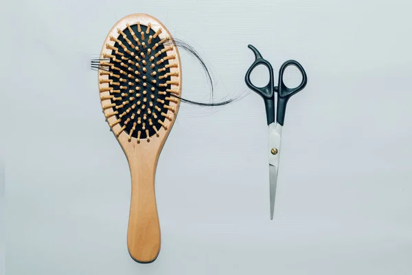 Wooden comb with fallen hair on it and scissors.