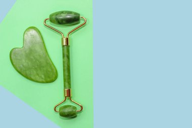 Yüz masajı yeşim taşı kazıyıcı ve soyut kağıt arka planda yüz silindiri.