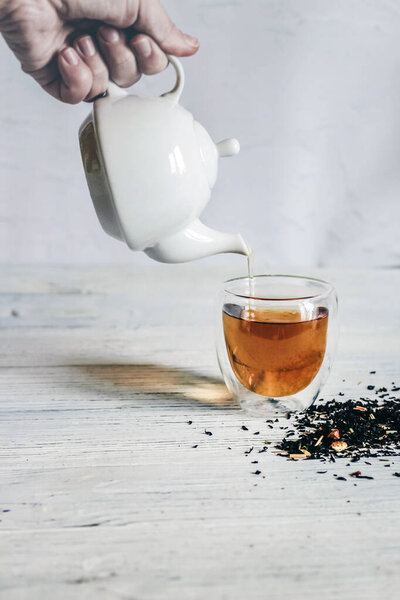 White decorative teapot pours tea into a glass.