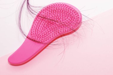 Karton bir arka planda taraklı pembe ve dökülen saçlar.