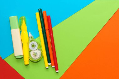 Çok renkli karton kağıdın arka planında sarı kırtasiye düzelticisi ve işaretleyiciler.