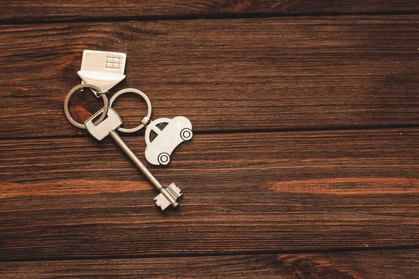 公寓的钥匙 钥匙串在房子的形状上 车在木制的背景上 — 图库照片