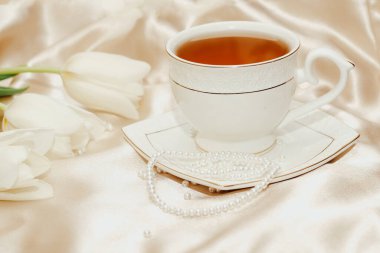 İnci boncuklu beyaz lale buketi ve ipek altın sarısı saten arka planda çay..