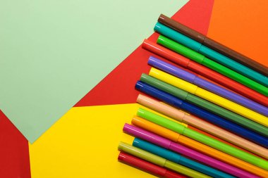 Çok renkli karton kağıdın arka planında keçeli kalemler var..