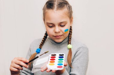 Bir kızın portresi, Ukrayna bayrağının mavi-sarı çizimi yanağında, elinde fırçayla resmedilmiş..