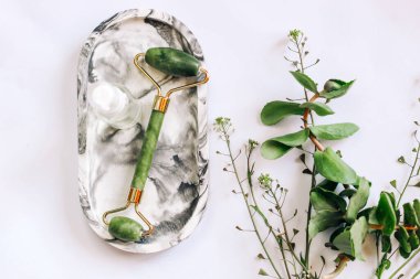 Yeşil bitkileri olan bir arka planda yeşim silindirli yüz masajcısı.