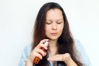 Kız saçının kabarık uçlarına kozmetik yağ sürüyor..