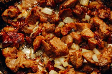 Fried pieces of meat with onions and seasonings in a frying pan close-up, meat goulash.