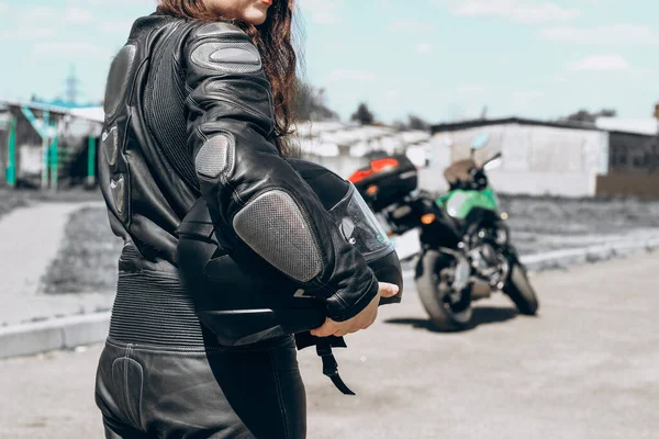 保護されたオートバイの革のスーツの女の子は彼女の背部でオートバイの背景に立つ — ストック写真