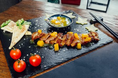 Mango soslu kızarmış domuz eti, domates, seramik siyah tabakta pide ekmeği.